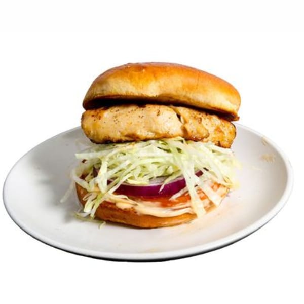 Grilled chicken burger with shredded lettuce, red onion, and sauce on a white plate.